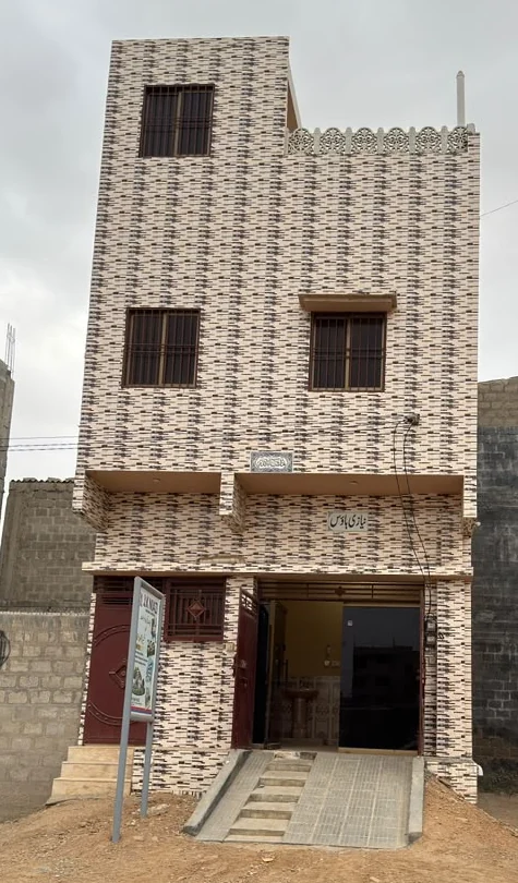 Front photograph of a narrow tiled residence with windows, entrance steps and a ramp