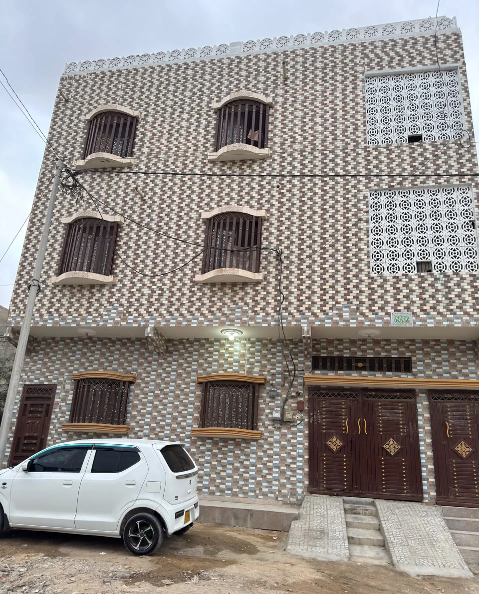 Front photograph of a tiled residence with arched windows, decorative screens and brown entrance gates